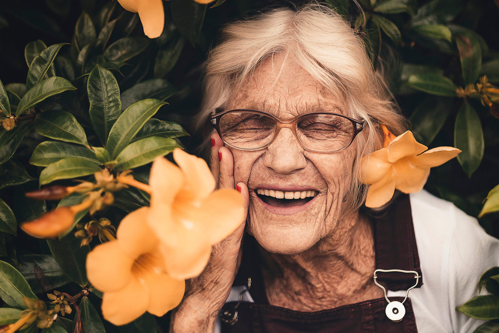 smiling elderly woman standing near yellow flowers